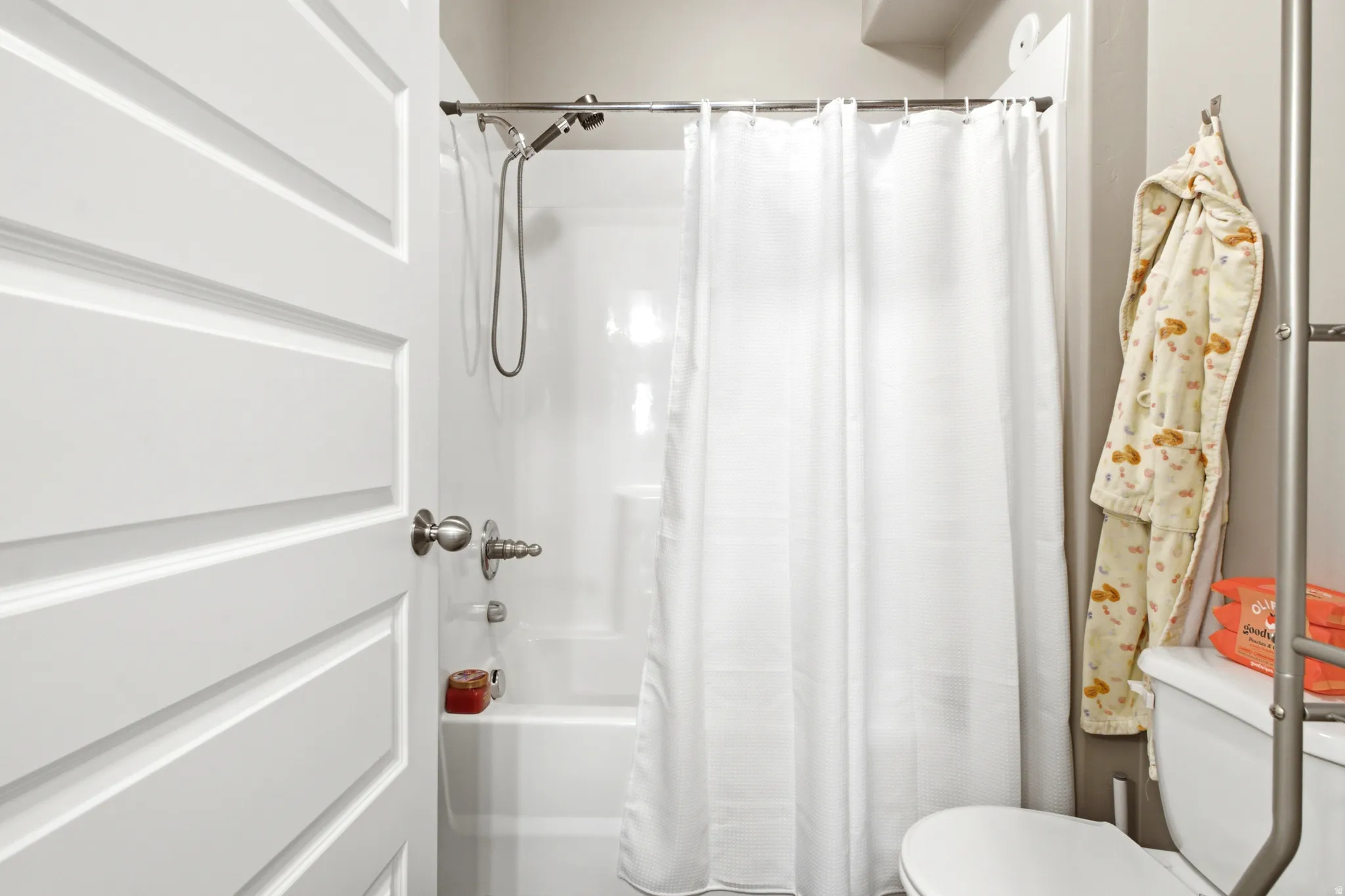 White paneled door with brushed nickel hardware opening to a bathroom featuring a white tub/shower combination, polished chrome shower fixtures, and a white toilet
