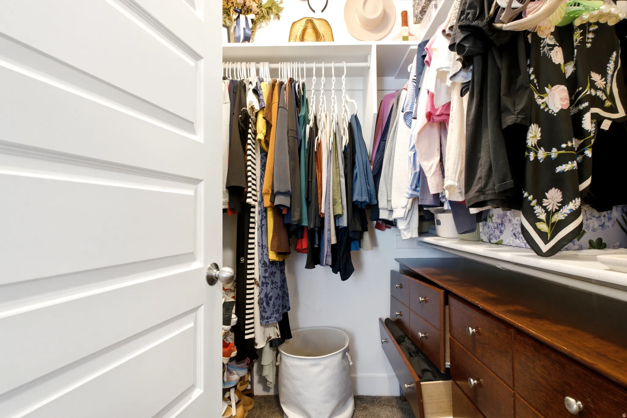 Walk-in closet featuring white shelving, multiple hanging rods, and built-in wood-finish drawers with brushed nickel hardware