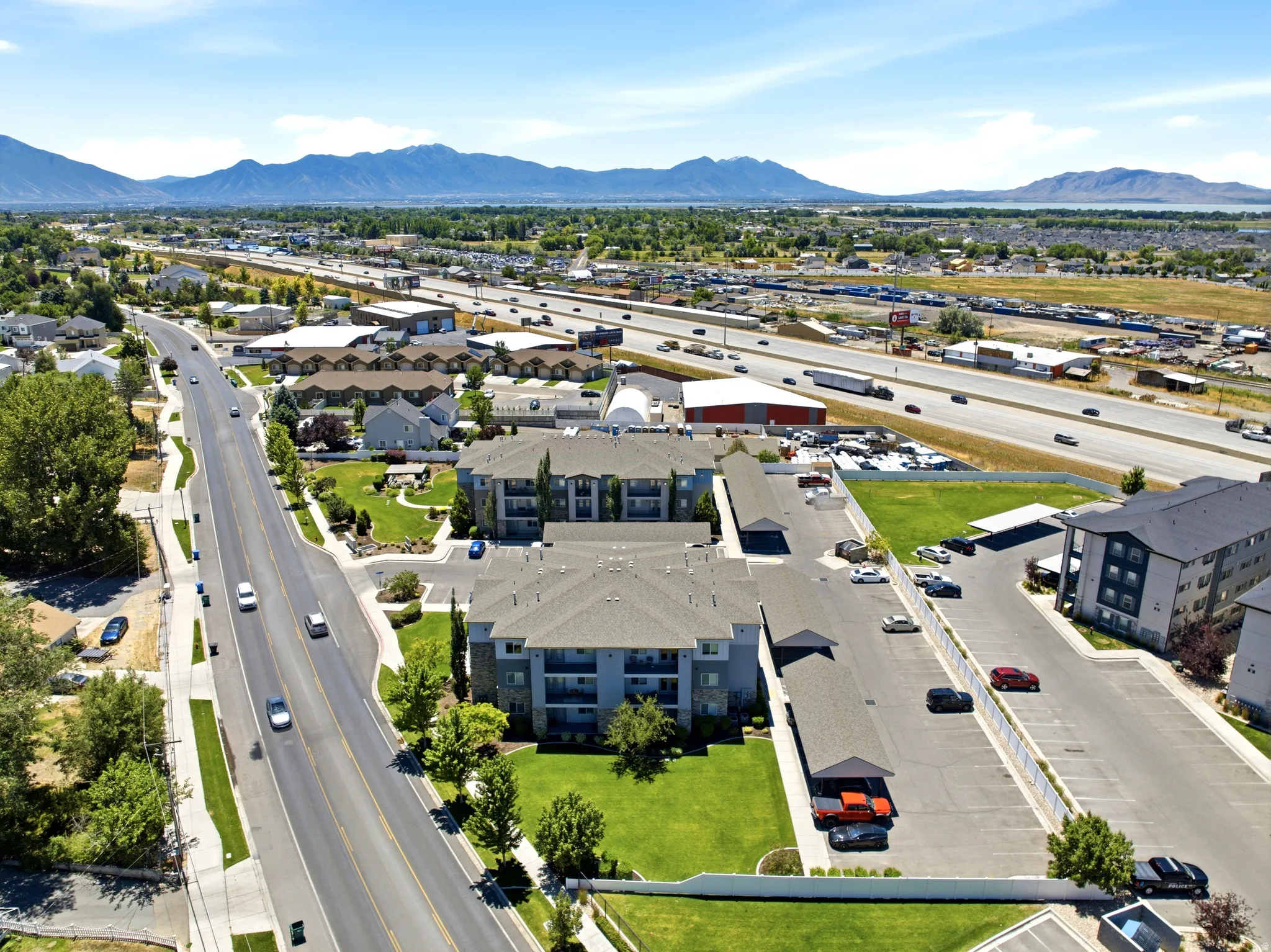 Aerial perspective of a multi-building apartment complex featuring covered parking, open-air parking, and green spaces