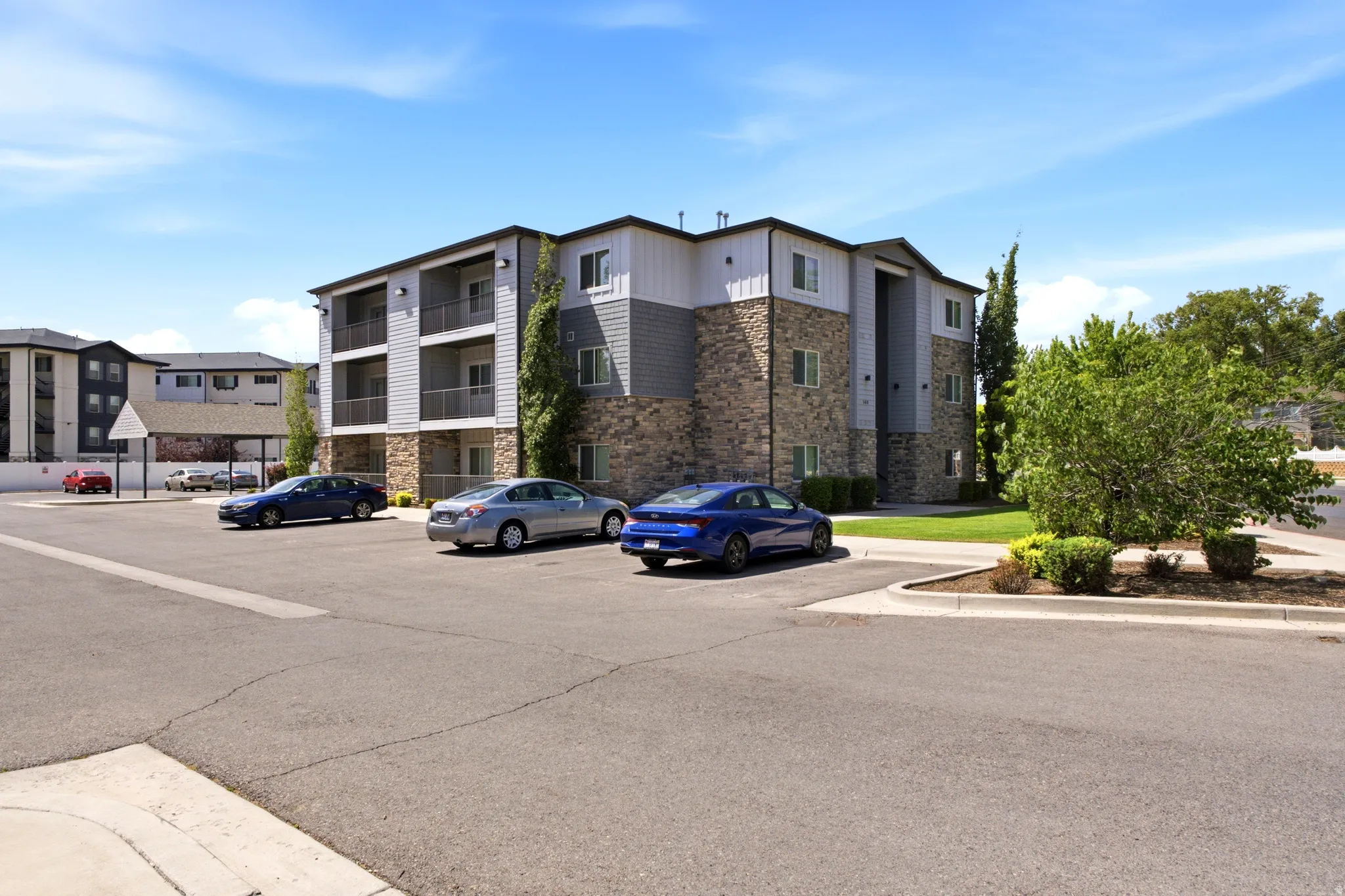 Multi-level building exterior featuring stone and siding finishes, multiple private balconies, and surrounding green landscaping