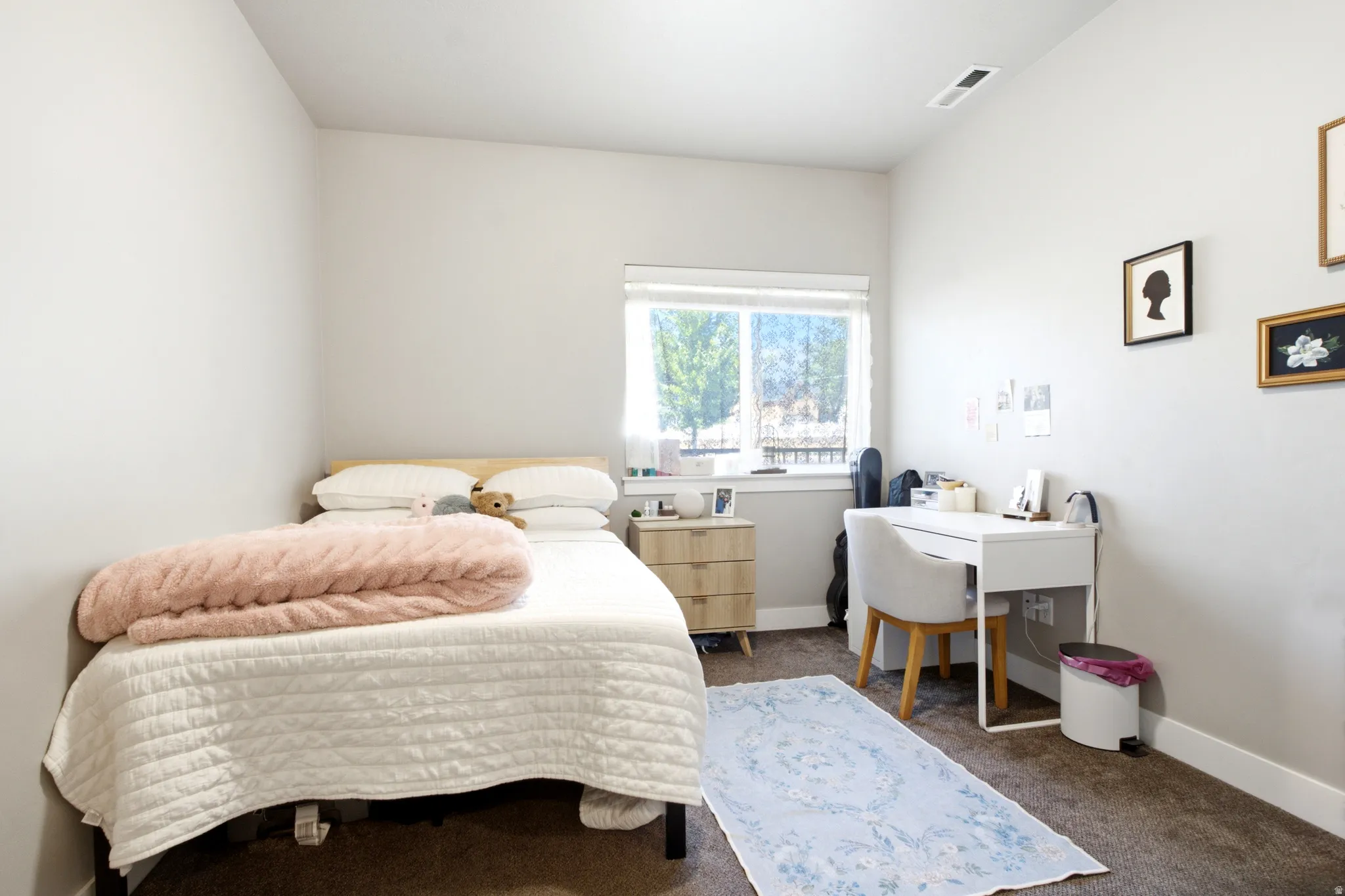 Bright room featuring a window with exterior views, light neutral wall paint, dark carpet flooring, and white baseboards