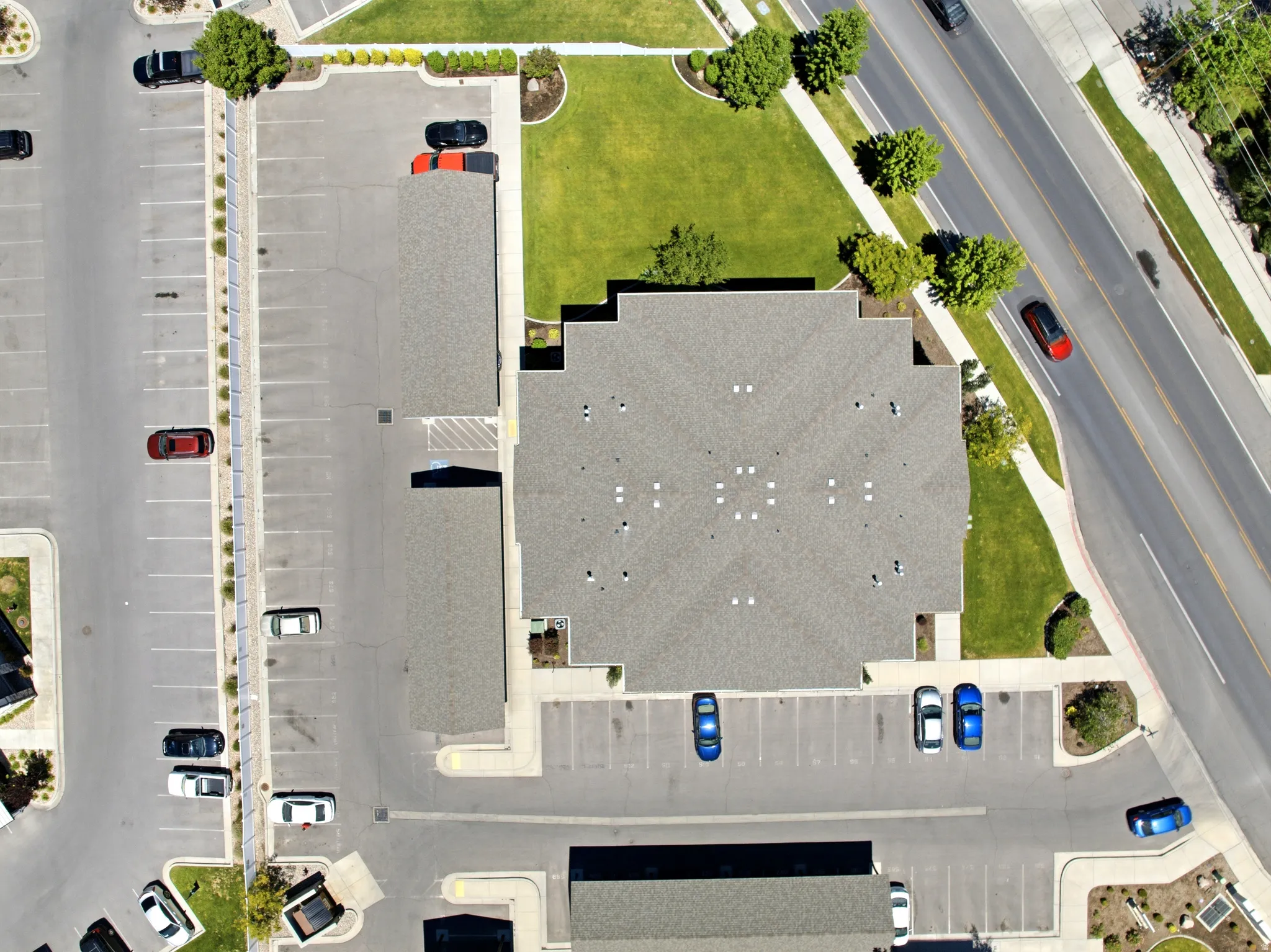 Commercial property featuring a large asphalt parking lot with marked spaces, extensive green lawn areas, and mature landscaping