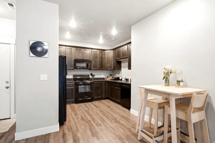 Full kitchen featuring dark wood cabinetry, black appliances, dark countertops, and wood-finish flooring