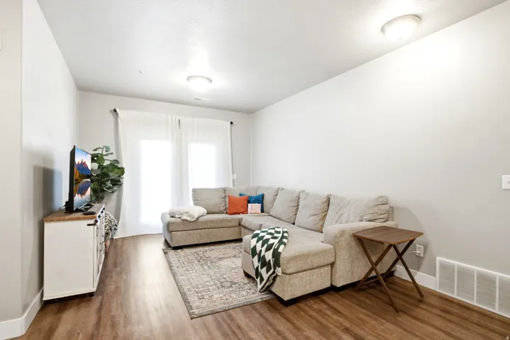 Living area featuring wood-finish flooring, light-toned walls, and a pair of large windows with sheer white curtains