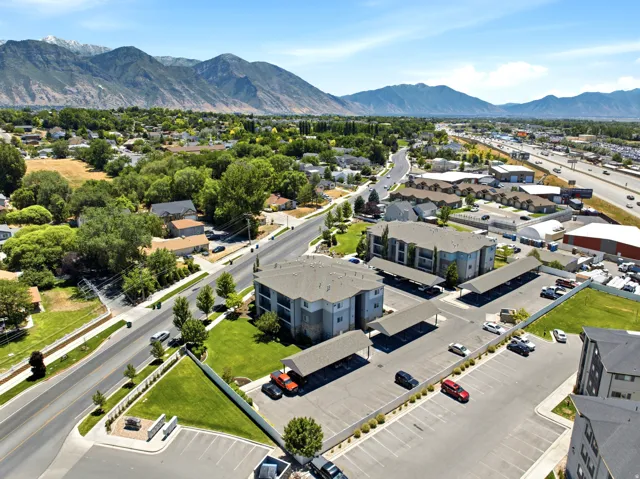 Apartment complex featuring covered parking, manicured green spaces, and a mountainous backdrop