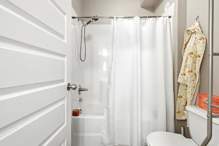 White paneled door with brushed nickel hardware opening to a bathroom featuring a white tub/shower combination, polished chrome shower fixtures, and a white toilet