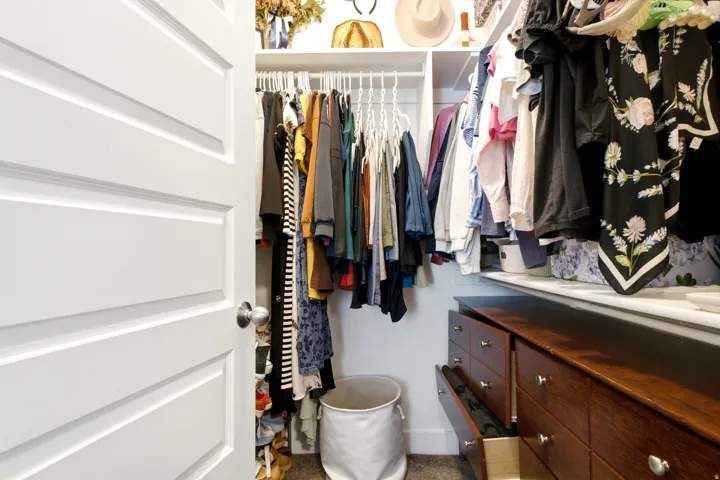 Walk-in closet featuring white shelving, multiple hanging rods, and built-in wood-finish drawers with brushed nickel hardware