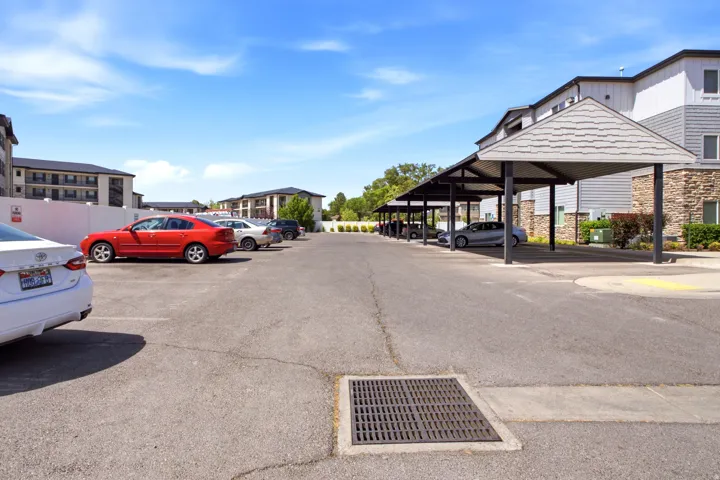 Expansive parking area featuring multiple covered carports, paved asphalt surfacing, and adjacent multi-level residential buildings with stone and siding exteriors