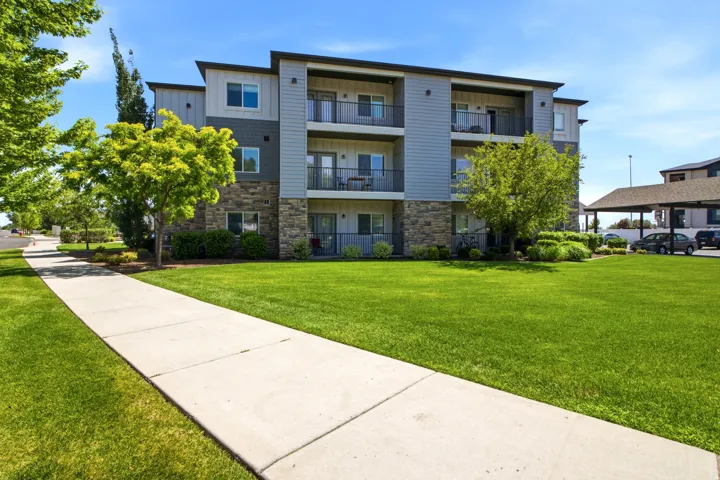 Contemporary multi-story building featuring stacked balconies with black railings, a stone facade on the lower level, and light siding on upper levels