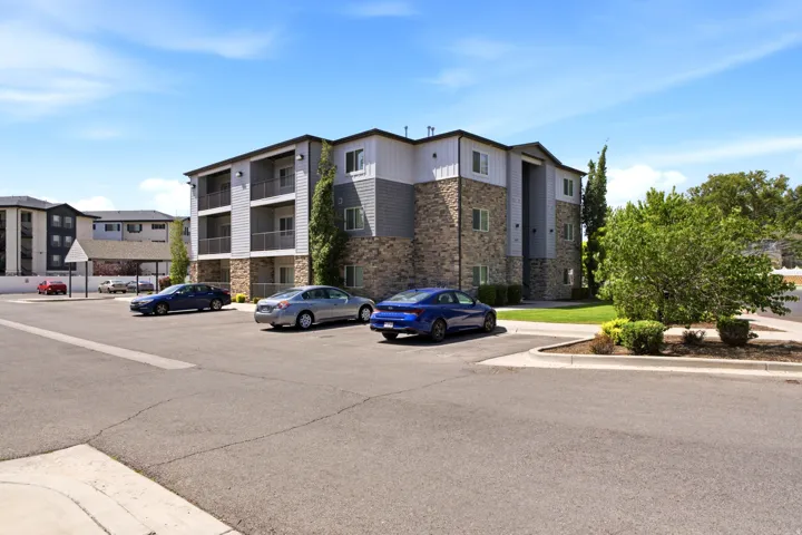 Multi-level building exterior featuring stone and siding finishes, multiple private balconies, and surrounding green landscaping