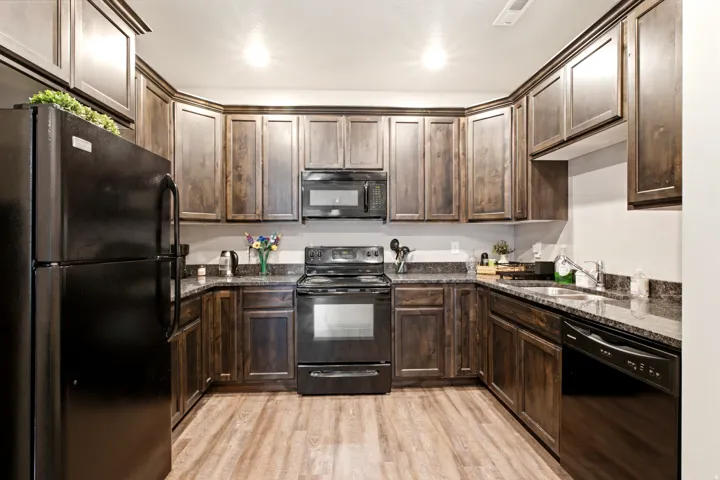 U-shaped kitchen featuring dark wood-finish cabinetry, granite-style countertops, wood-finish flooring, and black appliances including a refrigerator, stove, microwave, and dishwasher