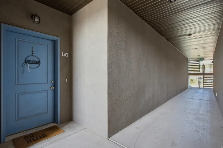 Entryway corridor featuring a blue panel door with a wall-mounted light fixture, textured wall finishes, a corrugated ceiling, and concrete flooring
