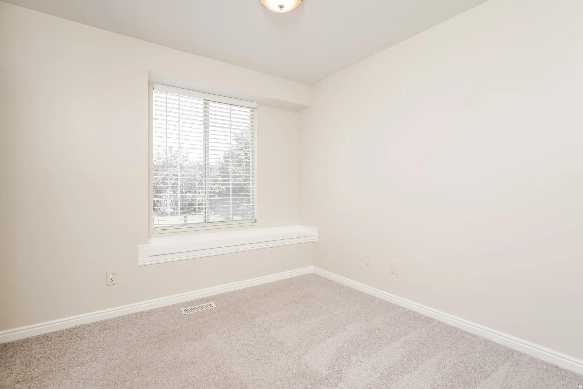 Neutral-toned room featuring a window with horizontal blinds, light beige carpeting, and white baseboards