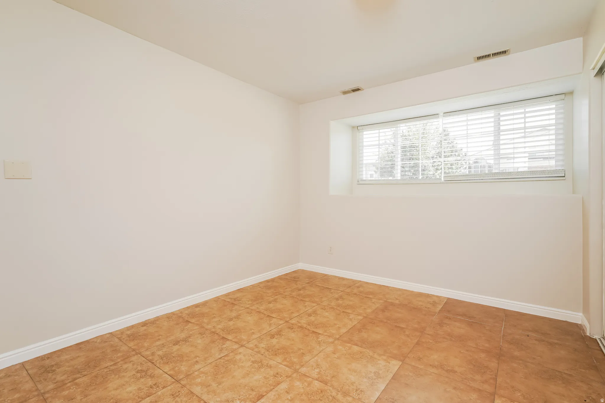 Room featuring neutral-toned walls, a large window with horizontal blinds, and ceramic tile flooring