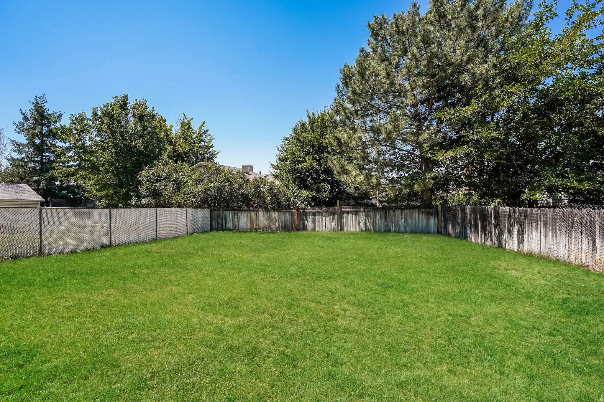 Expansive green lawn enclosed by chain-link and wood fencing, bordered by mature trees