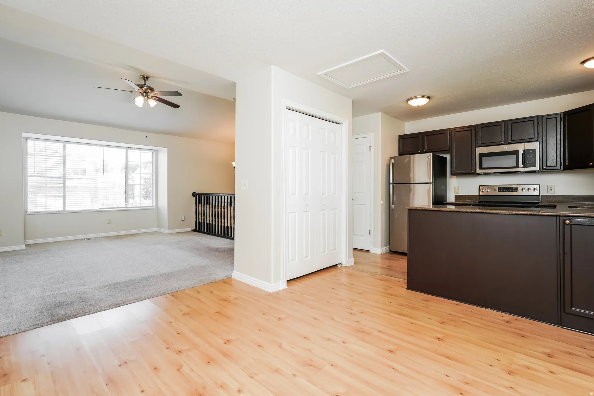 Open-concept living space featuring wood-finish flooring, a kitchen island with dark cabinetry, stainless steel appliances, and a dedicated dining area with a ceiling fan