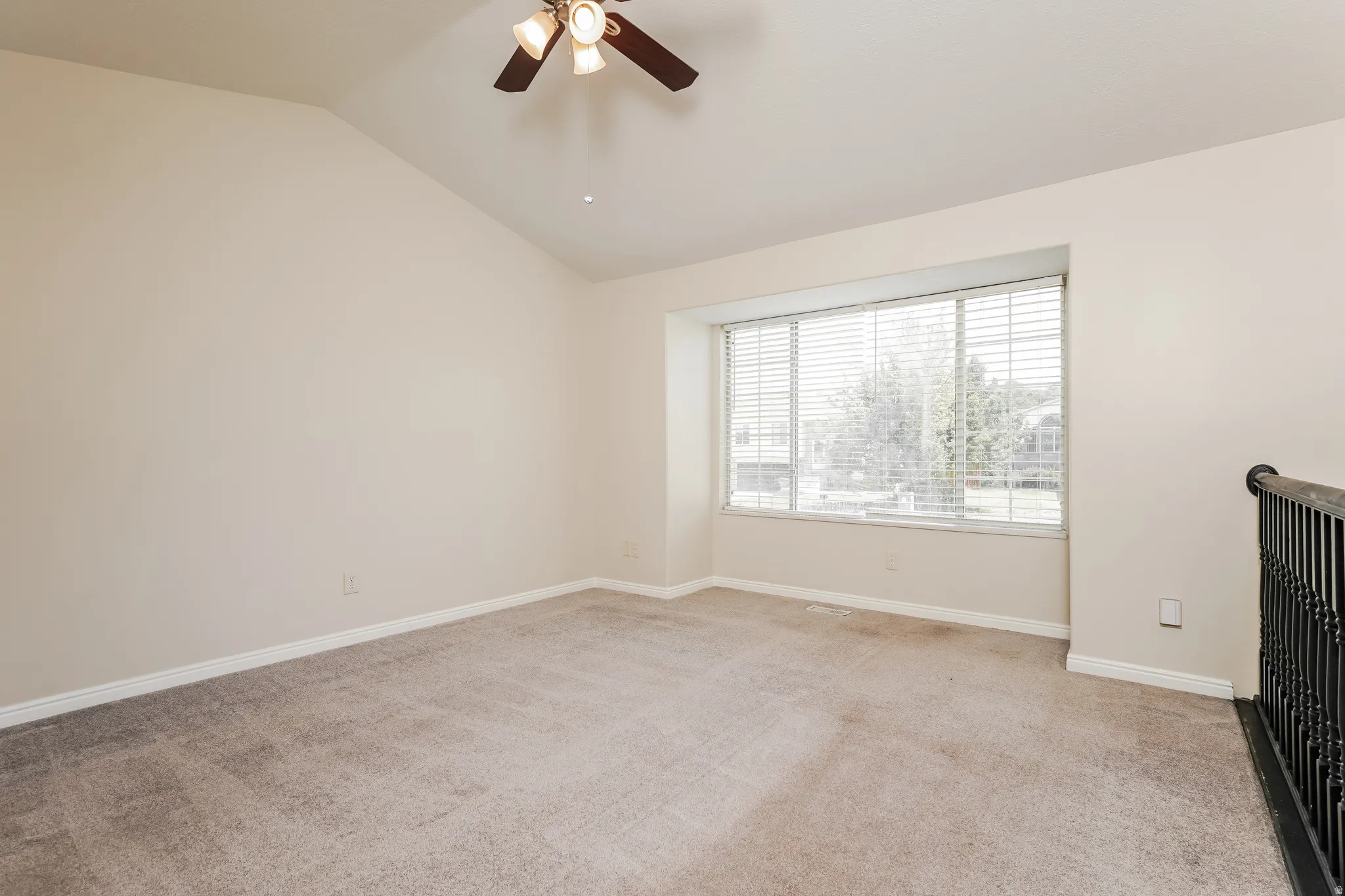 Spacious room featuring vaulted ceilings, a ceiling fan with integrated lighting, and a large window with horizontal blinds