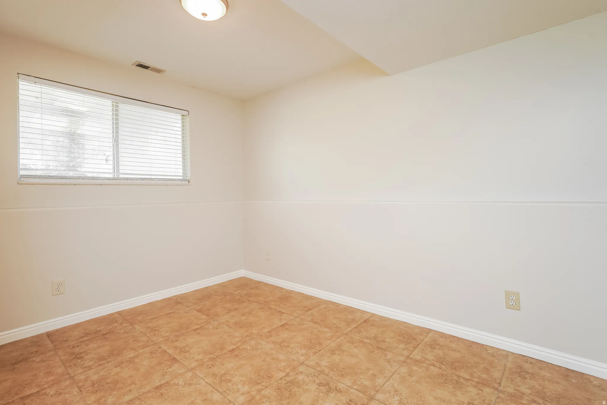 Bright room featuring a window with horizontal blinds, neutral wall paint with wainscoting detail, and large format square floor tiles