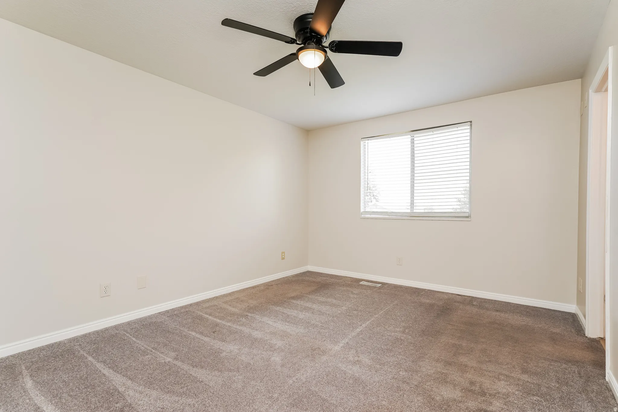 Carpeted room featuring a ceiling fan with integrated lighting, a window with horizontal blinds, neutral wall paint, and white baseboards