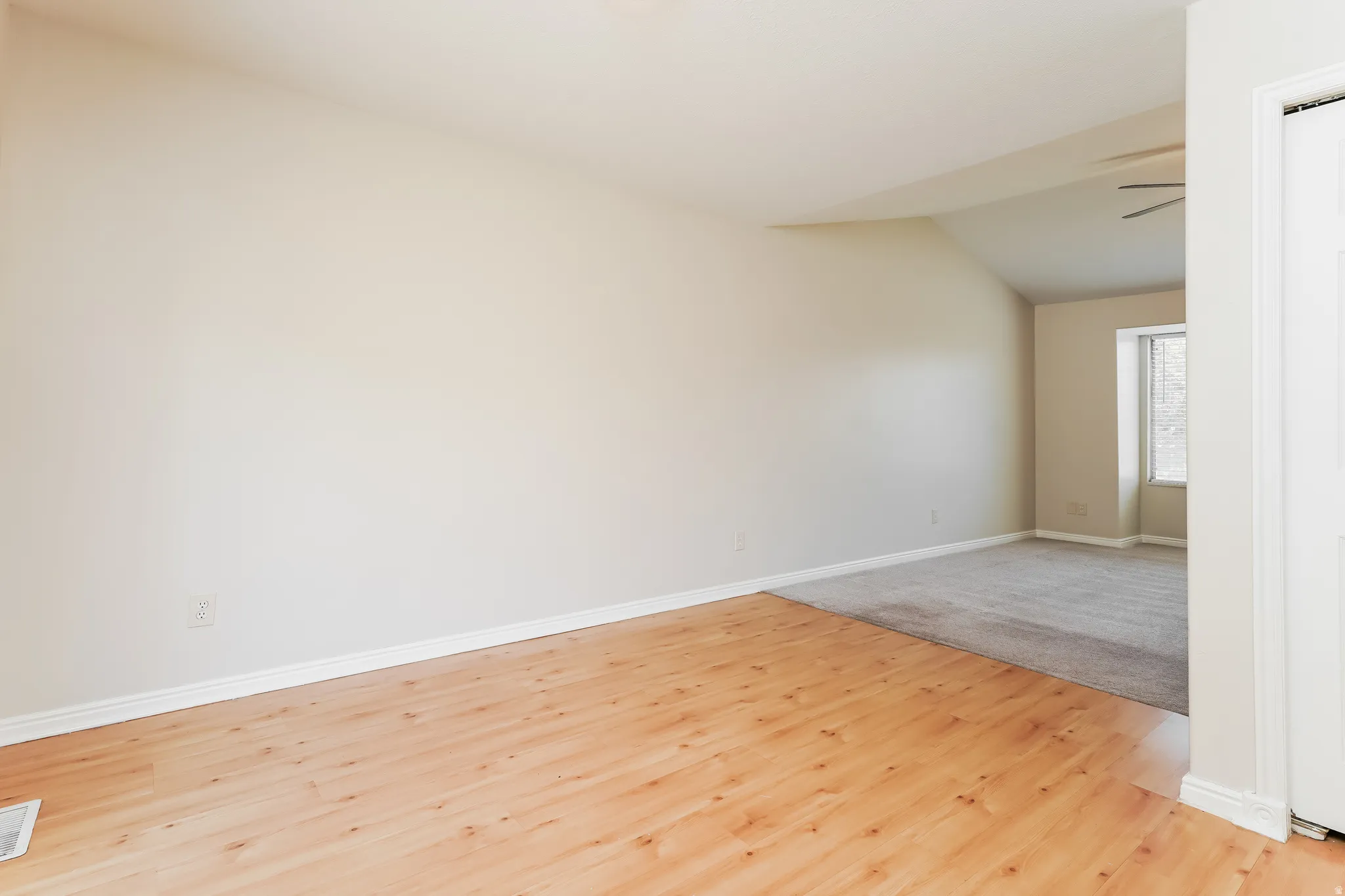 Spacious interior featuring wood-finish flooring transitioning to carpeting, a vaulted ceiling, and a ceiling fan