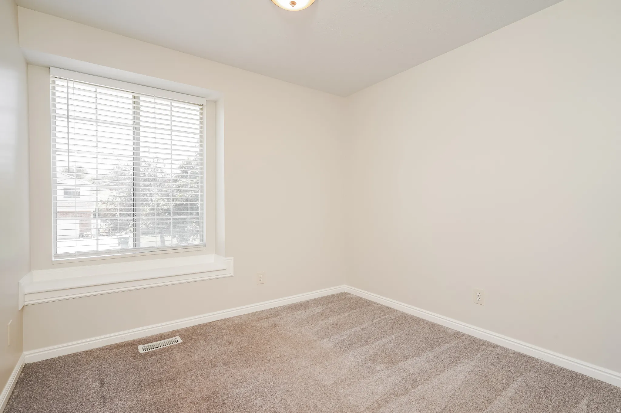 Bright room featuring neutral-toned walls, plush carpeting, a large window with white blinds, a window ledge, and white baseboards