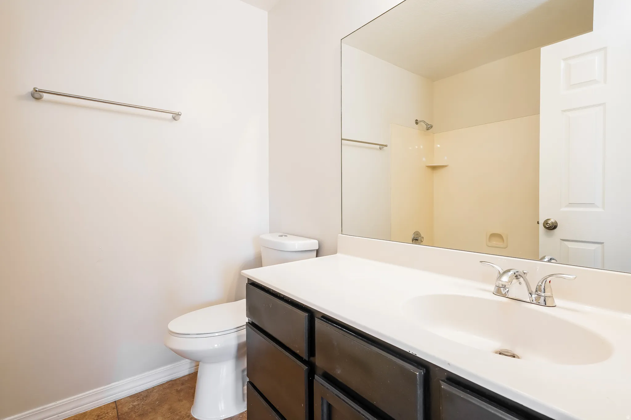 Bathroom featuring a dark wood-finish vanity with a white countertop, an integrated sink with chrome fixtures, a wall-mounted mirror, and tile flooring