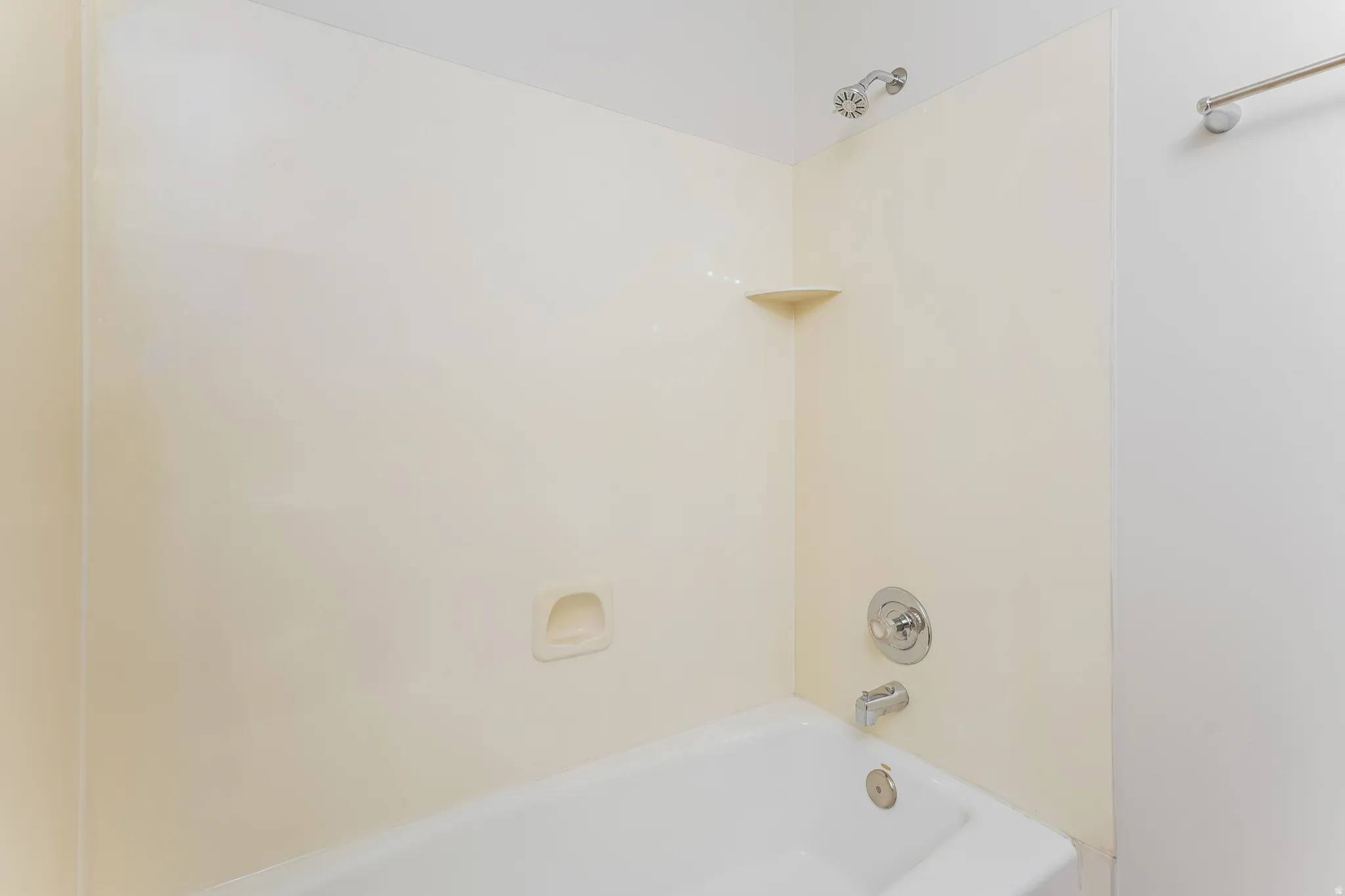 White bathtub with integrated shower, chrome fixtures, and a corner shelf