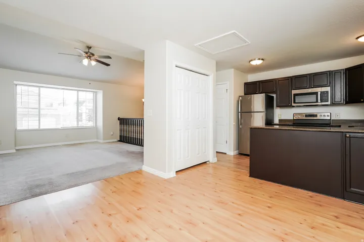 Open-concept living space featuring wood-finish flooring, a kitchen island with dark cabinetry, stainless steel appliances, and a dedicated dining area with a ceiling fan