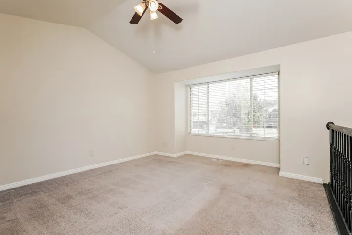Spacious room featuring vaulted ceilings, a ceiling fan with integrated lighting, and a large window with horizontal blinds