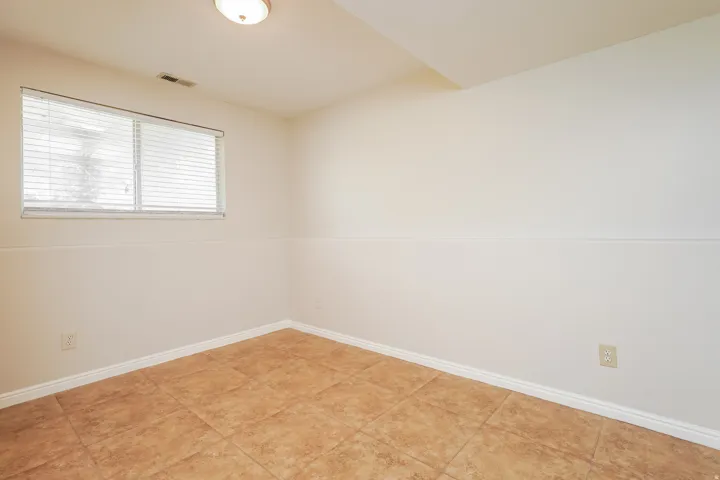 Bright room featuring a window with horizontal blinds, neutral wall paint with wainscoting detail, and large format square floor tiles
