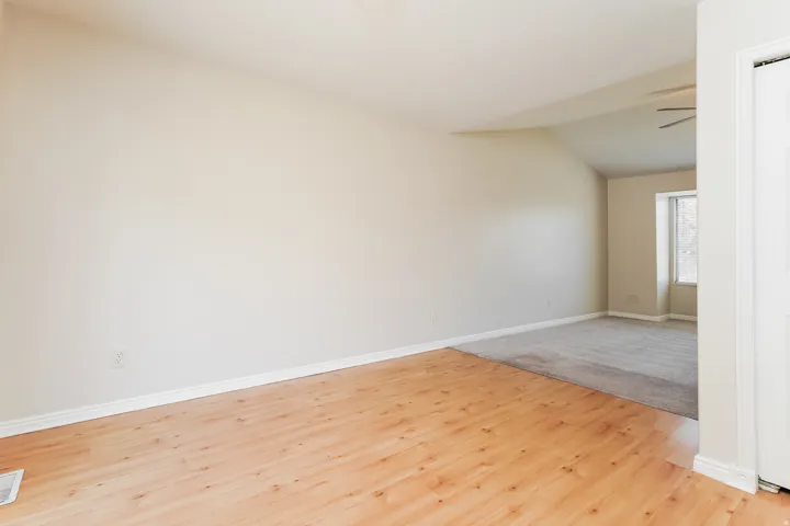 Spacious interior featuring wood-finish flooring transitioning to carpeting, a vaulted ceiling, and a ceiling fan