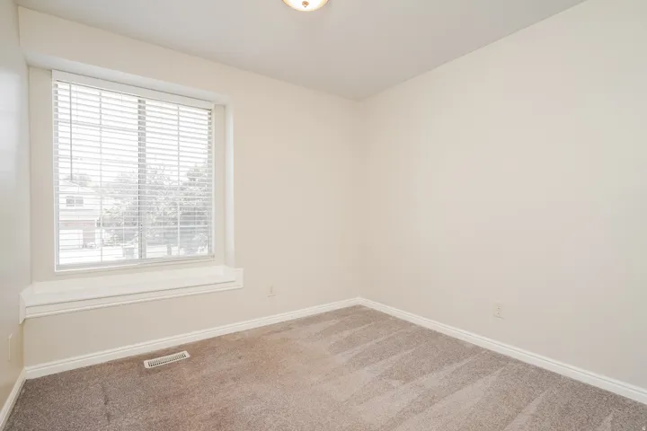 Bright room featuring neutral-toned walls, plush carpeting, a large window with white blinds, a window ledge, and white baseboards