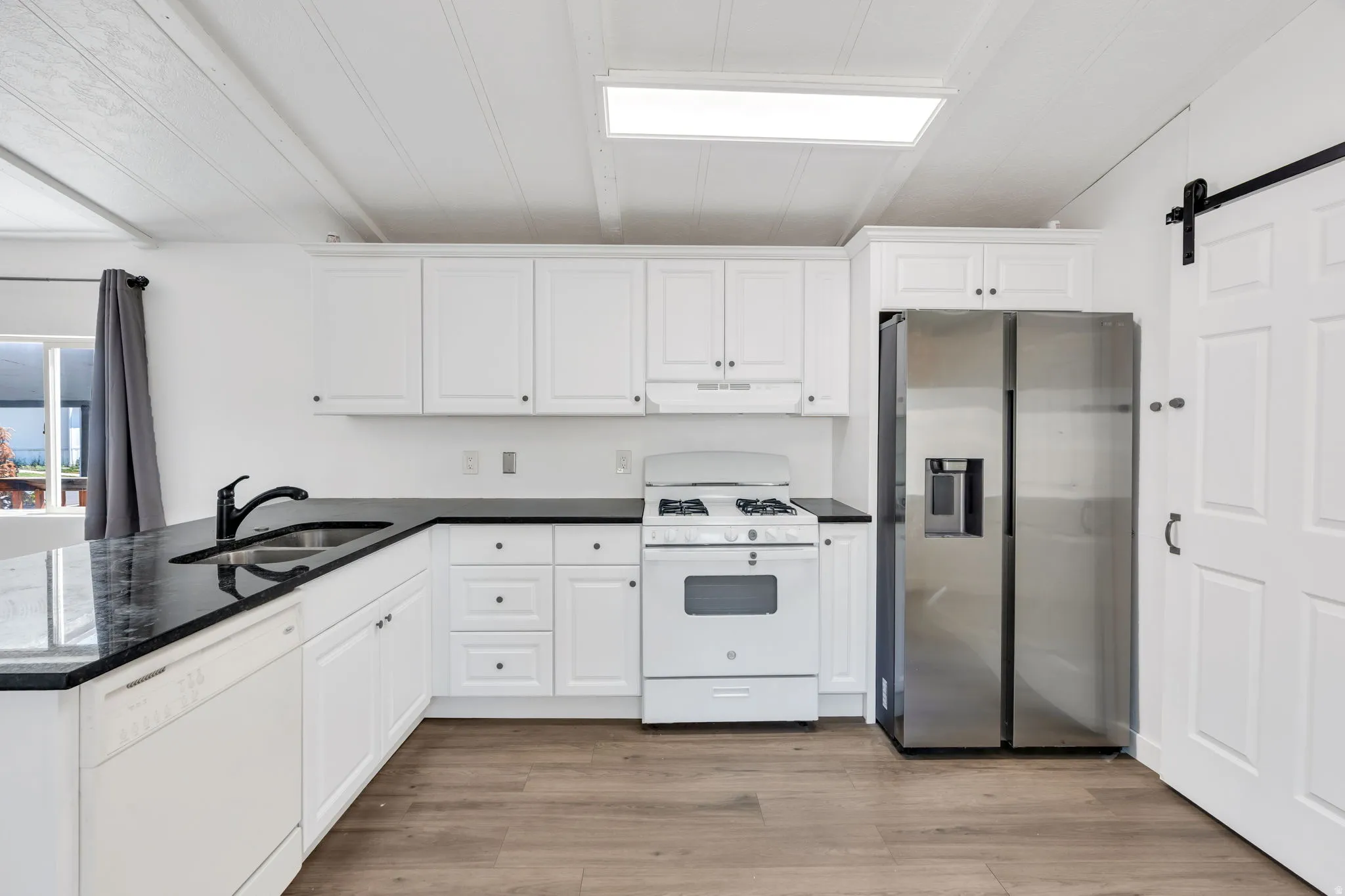 Kitchen featuring white cabinetry, dark countertops, a stainless steel refrigerator, and wood-finish flooring