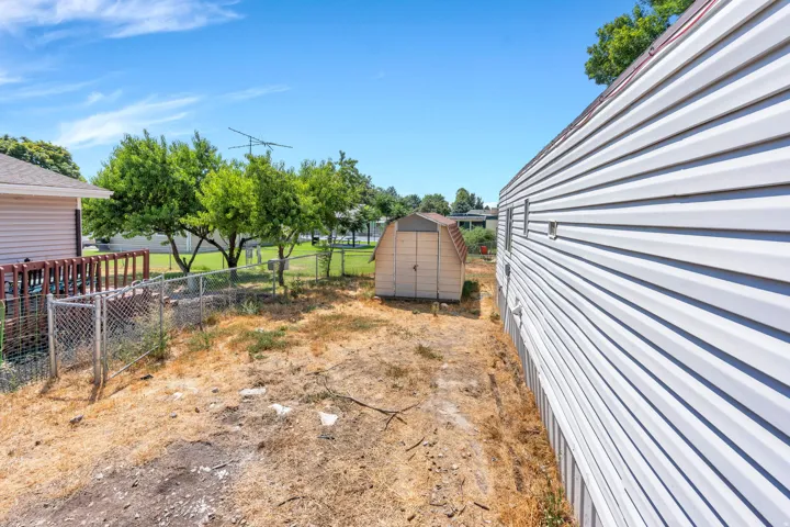 Detached storage shed, chain-link fencing, mature trees, and vinyl siding