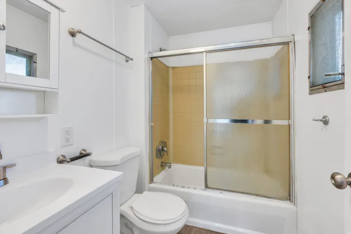 White vanity with integrated sink, white toilet, and tub with sliding glass enclosure