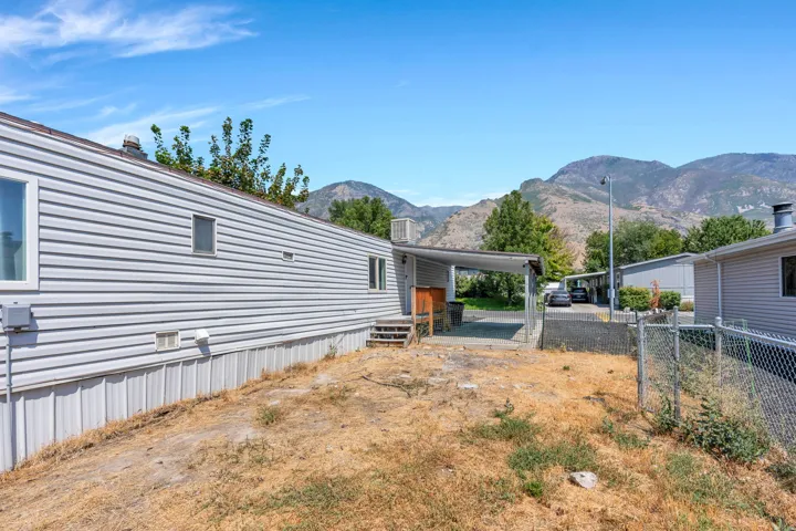 Mountain backdrop with a clear sky, featuring a property with light-colored siding and a covered carport