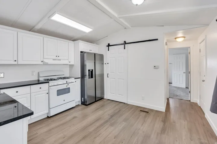Kitchen featuring white cabinetry, dark countertops, wood-finish flooring, stainless steel refrigerator, and a sliding barn door