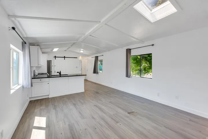 Vaulted ceiling with skylight, wood-finish flooring, white cabinetry, dark countertops, and a barn door