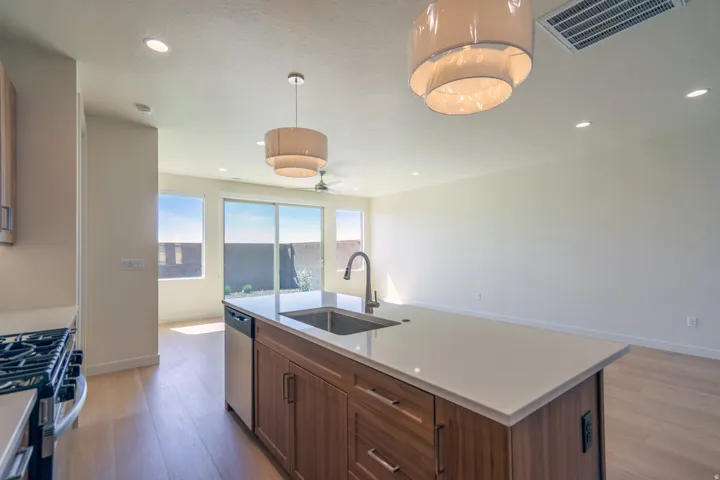 Kitchen island featuring a stainless steel sink with a gooseneck faucet, light-toned countertop, and wood-finish cabinetry