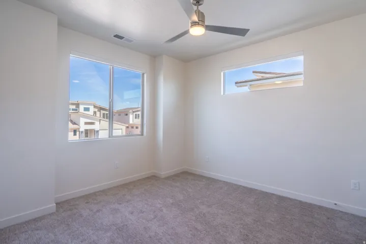 Bright bedroom featuring dual windows with expansive natural light, neutral carpet flooring, and ceiling fan with integrated lighting fixture