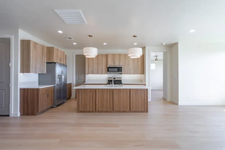 Open-concept kitchen featuring wood-finish cabinetry, stainless steel appliances, a center island with sink, and light wood-finish flooring