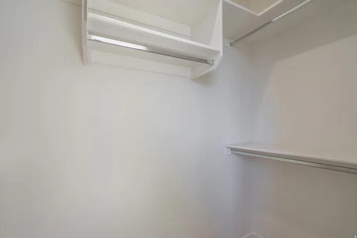 Walk-in closet featuring white painted walls, multiple white shelving units, and chrome hanging rods