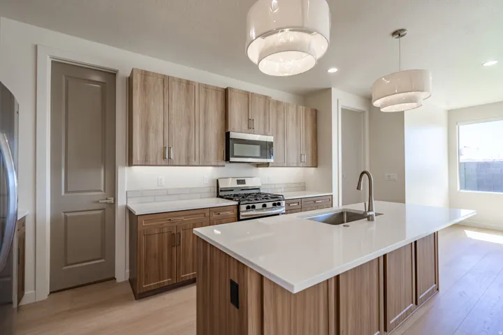 Kitchen featuring a large island with an undermount sink, light wood-finish cabinetry, stainless steel appliances, white subway tile backsplash, and light wood-finish flooring