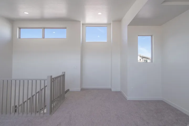 Bright, open loft-style space featuring soaring ceilings with recessed lighting, expansive windows flooding the area with natural light, and neutral carpet flooring