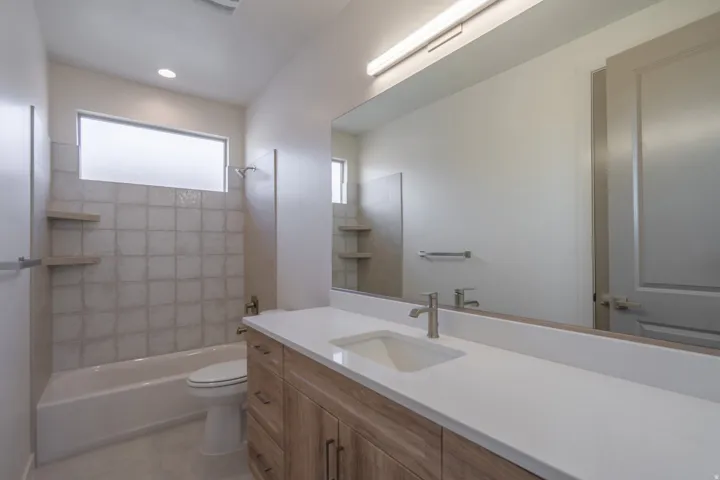 Bathroom featuring a wood-finish vanity with a white countertop and integrated sink, a large mirror, and a tub-shower combination with square tiled surround and built-in shelving