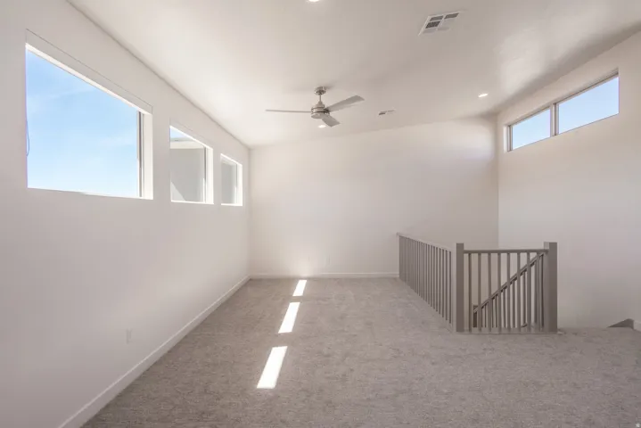 Spacious carpeted room featuring a contemporary ceiling fan, recessed lighting, and multiple windows