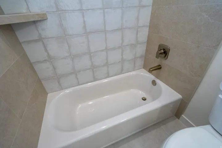 White bathtub with brushed nickel fixtures, complemented by light-toned wall and floor tiling