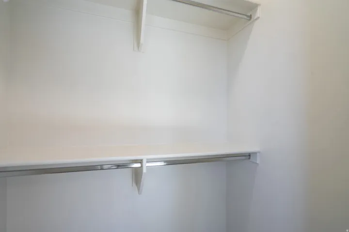 White painted closet interior featuring multiple shelving units and chrome hanging rods