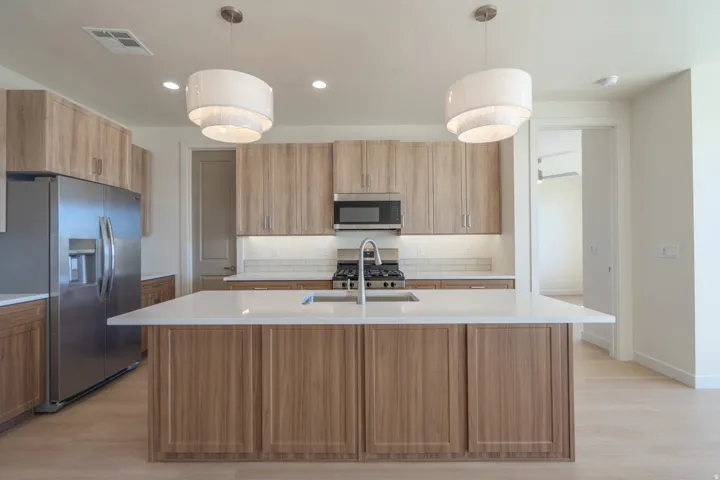 Modern kitchen featuring a central island with a white countertop and undermount sink, complemented by wood-finish cabinetry
