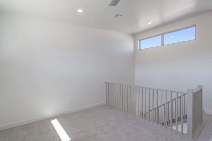 Carpeted loft area featuring a light gray baluster railing, recessed lighting, and high transom windows